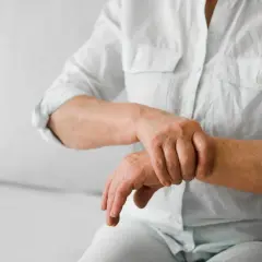 Osoba w białej koszuli masuje nadgarstek, odczuwając ból stawów.