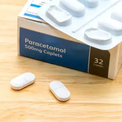 Opakowanie Paracetamolu 500mg, leki na ból kręgosłupa szyjnego, leżą na drewnianym blacie obok dwóch tabletek.