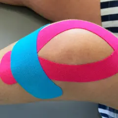 Kolano z różowym i niebieskim plastrem kinezjotapingowym, łagodzącym ból nad kolanami.