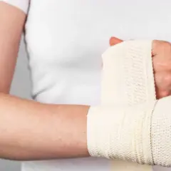 Osoba owija rękę bandażem. Widoczne są objawy stłuczenia nadgarstka: ból, obrzęk i ograniczenie ruchomości.