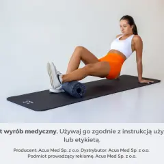 Kobieta pokazuje, jak się rolować na macie z użyciem wałka do masażu.