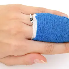 Zwichnięcie palca u ręki, opatrzony niebieskim bandażem, z pierścionkiem z czarnym kamieniem.