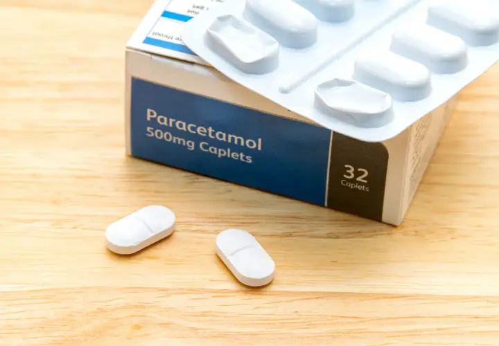 Opakowanie Paracetamolu 500mg, leki na ból kręgosłupa szyjnego, leżą na drewnianym blacie obok dwóch tabletek.