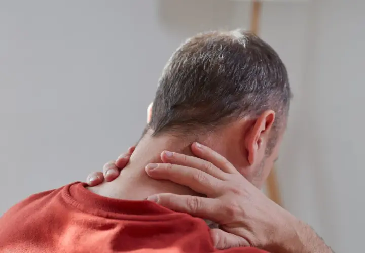 Mężczyzna masuje kark, szukając ulgi w bólu. Rozważa wdowi garb ćwiczenia w domu, by poprawić postawę.