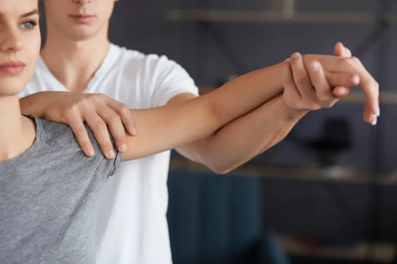 Fizjoterapeuta bada rękę pacjentki, która odczuwa ból łokcia promieniujący do dłoni.