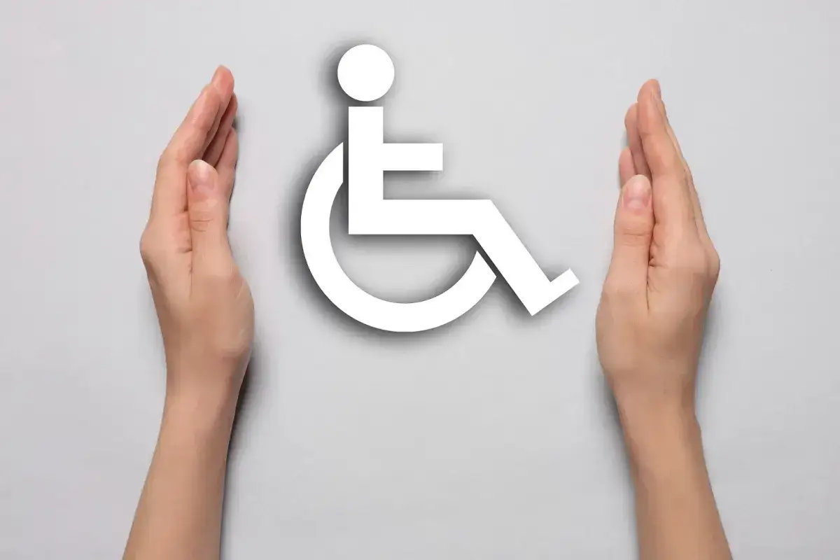 Dwie dłonie otaczają symbol osoby na wózku inwalidzkim, symbolizując wsparcie dla osób z chorobą Scheuermanna, która może prowadzić do grupy inwalidzkiej.