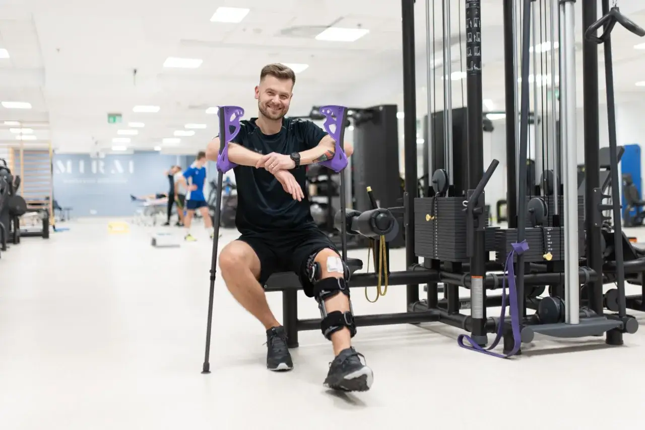 Mężczyzna z kulami łokciowymi i ortezą na kolanie, rehabilitujący się po bólu łąkotki przyśrodkowej.