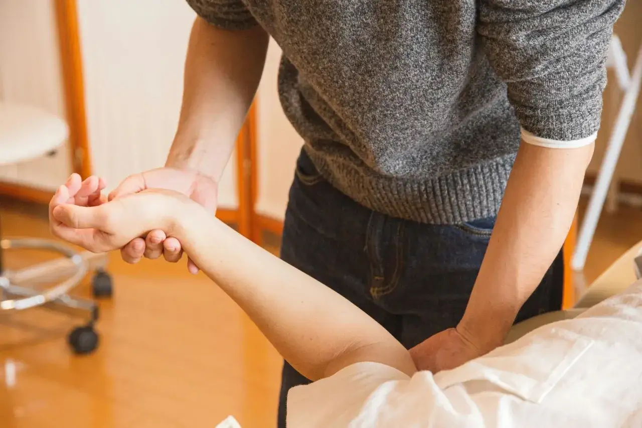 Fizjoterapeuta pomaga w rehabilitacji ręki po złamaniu kości promieniowej, delikatnie masując przedramię pacjenta.